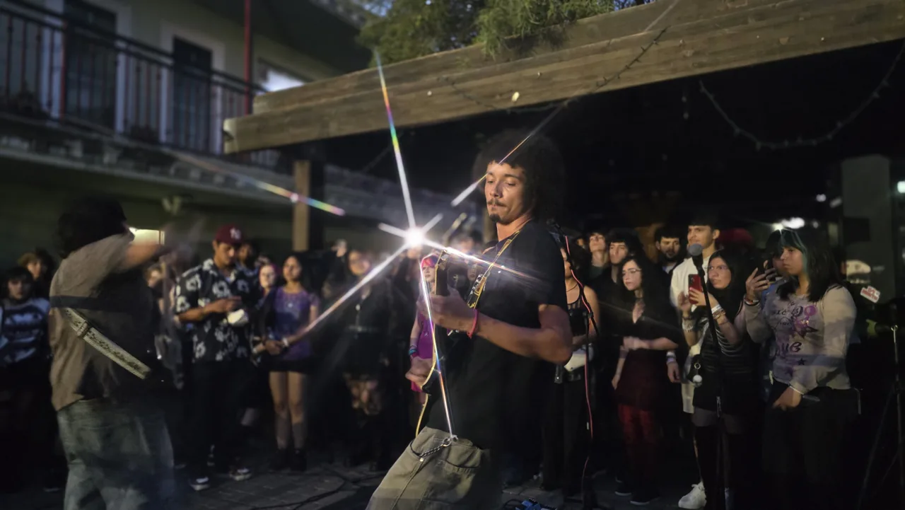 A guitarist playing among the crowd in a courtyard, with light flaring off the guitar