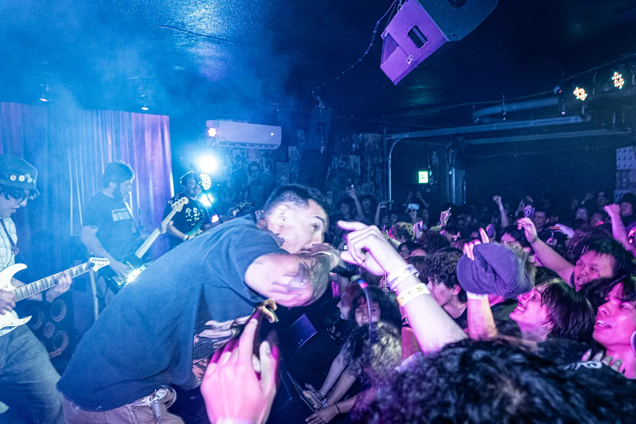 A vocalist leaning into a packed crowd under blue and pink stage lights